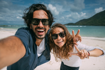 A pair of lovers take a selfie on a tropical beach. - obrazy, fototapety, plakaty