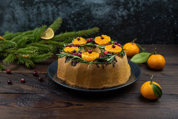 Tangerine ring cake decorated with sliced mandarines, cranberries and rosemary on wooden background.