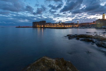 Sunset and Night view of Dubrovnik old town from seaside with reefs in foreground, Croatia