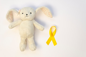 Top view teddy rabbit with a yellow ribbon on a white table with copy space. Childhood Cancer Awareness day February, 15 concept
