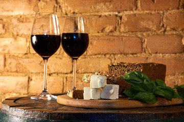 Two glasses of red wine, few pieces of rye bread, cheese and basil