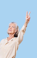 Senior woman in casuals gesturing peace sign against blue background