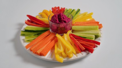 Vegetable plate on a white table with beetroot paste. Sliced bell peppers, cucumbers and carrots.    