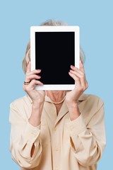 Senior woman holding tablet PC in front of her face against blue background