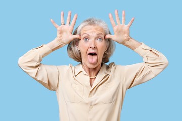 Portrait of senior woman making funny faces with hands on head against blue background