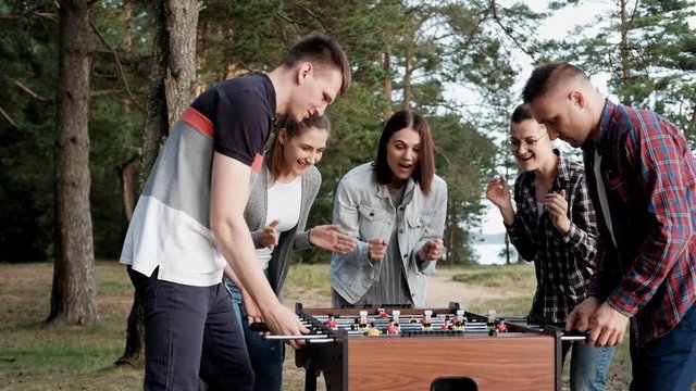 Friends play table football or kicker outdoors. A party in nature. Players and fans rejoice in the victory.
