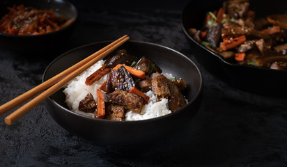 Vegan Korean seitan, carrot and eggplant fry over rice with kimchi in a black bowl