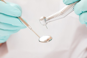 Dentist's hands in gloves with dental handpiece and mouth mirror.