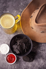 Mexican corn chips nachos, glass of beer and cowboy hat. Black chips nachos for brutal men.
