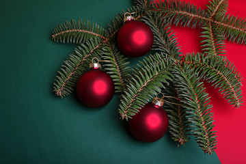 A branch of blue spruce with red christmas balls on a red and green background. Copy space.