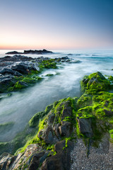 Obraz premium Impressive sunrise in a beach of Malaga, Andalusia with long exposure water and green rocks in firts place