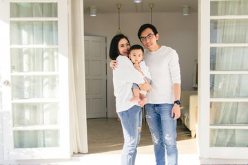 Portrait of an Asian family consisting of parents and babies happily hugging in front of his house.