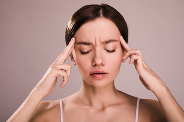 Fototapeta premium Disturbed worried young woman keep eyes closed and fingers close to head. Has headache or pain. Suffer from discomfort. Young model without pain relief. Isolated over beige background.
