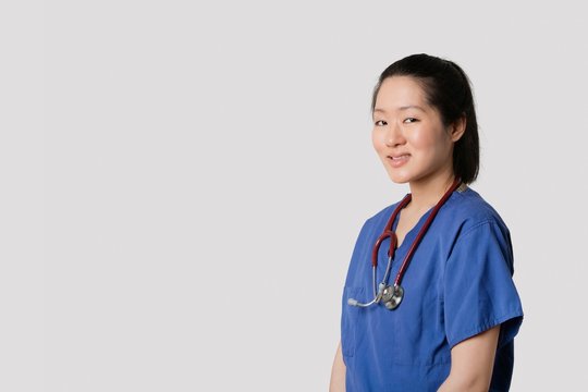 Portrait Of A Young Asian Female Surgeon Smiling Over Gray Background