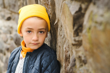 Stylish kid wears yellow hat nad warm jacket. Face portrait of cute boy. Kids fashion