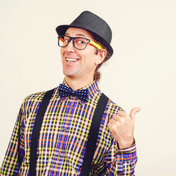 Smiling nerd man in bow tie and suspenders is showing thumbs up. Happy geeky hipster wears retro hat and clothes. Gesturing OK