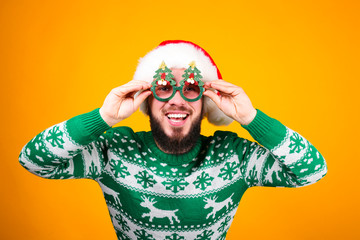 Studio portrait of handsome bearded man wearing christmas sweater with snowflake ornament, posing over the yellow wall, copy space for text. Festive background. Male with facial hair smiling.
