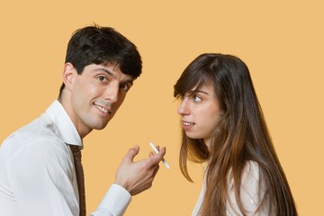 Portrait of a young man with cigarette while woman looking at him over colored background