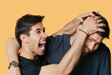 Young male friends playfighting over colored background