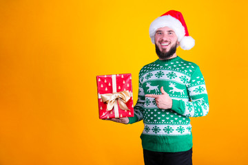 Studio portrait of handsome bearded man wearing christmas sweater with snowflake ornament, posing over the yellow wall, copy space for text. Festive background. Male with facial hair smiling.