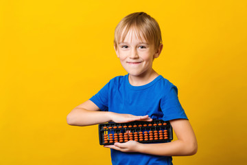 Cute boy holding abacus for learning mental mathematics. Smiling boy over yellow background