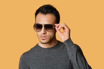 Stylish young man wearing sunglasses over colored background