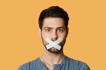 Portrait of a young man with tape on mouth over colored background