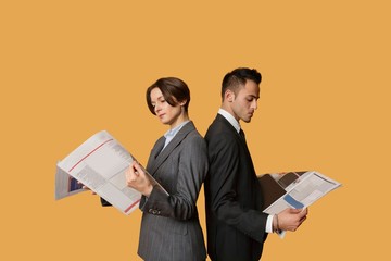 Business partners standing back to back while reading newspaper