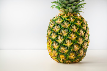a whole ripe pineapple stands on a white surface with a light gray background.