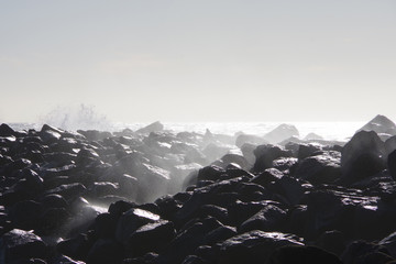 A field of rocks on the open California ocean shore being sprayed by splashing waves on a windy...