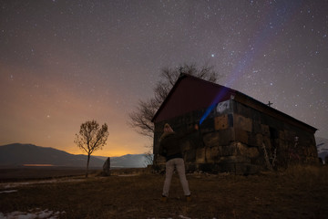 Beautiful night landscape, a girl with a flashlight stands at a small church. A colorful star in...