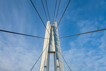 Fototapeta premium White metal poles and steel ropes of a suspension pedestrian bridge against a blue sky. They remind you of a web.