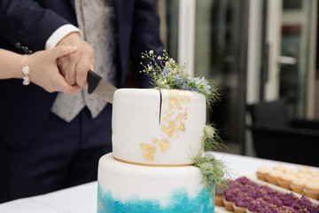 Braut und Bräutigam schneiden moderne Hochzeitstorte mit aquarell fondant und blattgold an
