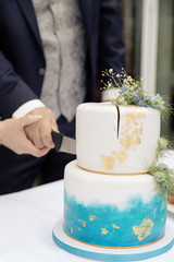 Braut und Bräutigam schneiden moderne Hochzeitstorte mit aquarell fondant und blattgold an
