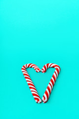 Two sweet caramel striped cane festive folded in the shape of a heart on a blue turquoise background. Holiday neo concept of Christmas and Valentine's Day. Vertical composition