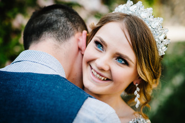 Stylish happy bride, woman with crown and groom, man. Newlyweds are hugging and kiss. Close up. On the background of nature. Weddings, engagement, marriage proposal, dating.