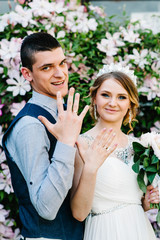 Stylish happy bride with bouquet of peonies with crown and groom. Newlyweds display golden wedding...