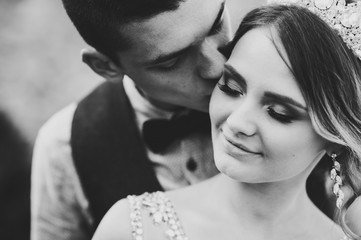 Stylish happy bride, woman with crown and groom, man. Newlyweds are hugging and kiss. Close up. On the background of nature. Black and white photo