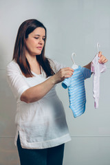 Pregnant woman choosing pink or blue baby bodysuits indoor
