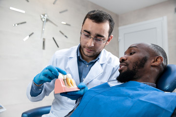 Young african-american man visiting dentist's office for prevention and treatment of the oral cavity. Man and male doctor while checkup teeth. Healthy lifestyle, healthcare and medicine concept.