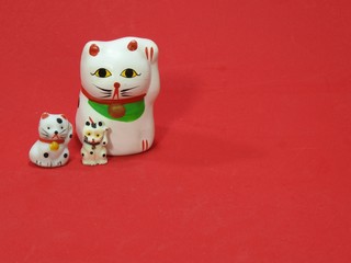 Three little Maneki Neko, Japanese lucky cats, amulets that bring good luck, protection, prosperity, health and happiness. They look like father (mother) and sons. Red background.