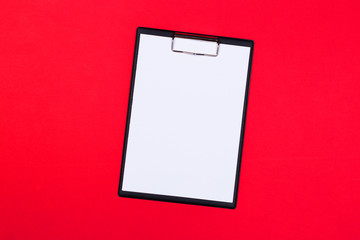 Clipboard with white sheet and pen on a red background. View from above. space for text
