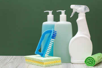 Bottles of dishwashing liquid, glass and tile cleaner and sponges on green background.