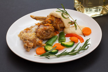 Rabbit legs baked in white wine with bechamel sauce on a ceramic plate with vegetables and rosemary.