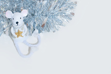 white festive toy of mouse or rat on the white background with silver shiny tinsel behind.
