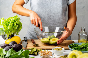 Woman mashing avocado with a fork, cooking guacamole in a glass bowl. healthy food concept.
