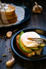 Avocado poached egg on a golden crouton with garlic and pepper. In the background are the loafs of waxed paper. Vegan Healthy Eating.