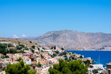 Fototapeta na wymiar Amazing view on tiny colorful houses on rocks and oleander trees near the Mediterranian sea on Greek island in sunny summer day, vacation on exotic islands