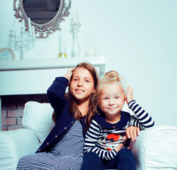 two cute sisters at home playing, little smiling girl in house interior on sofa, messing hair,...
