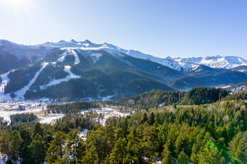 Obraz premium Winter sunny landscape with snowy peaks of mountain ranges with green trees and blue sky